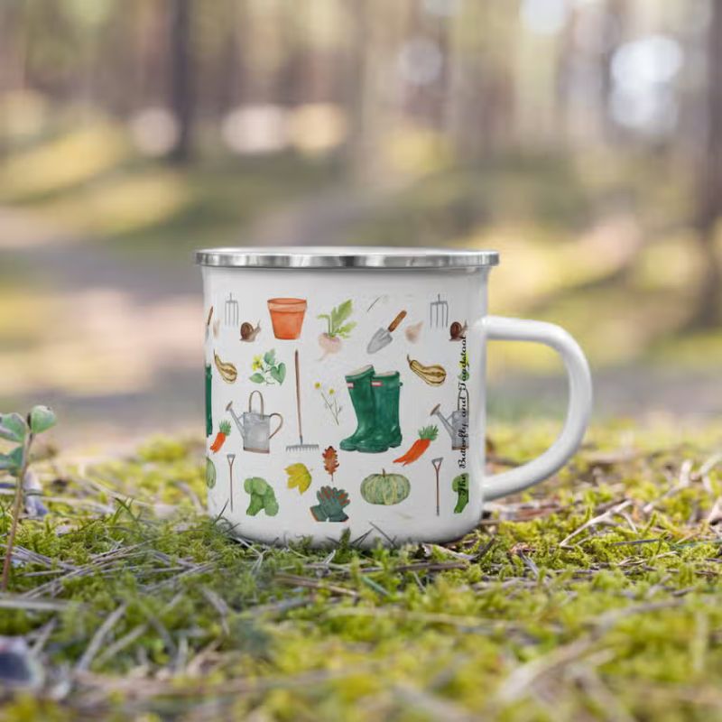 An enamel mug with watercolour gardening motifs including green wellingtons