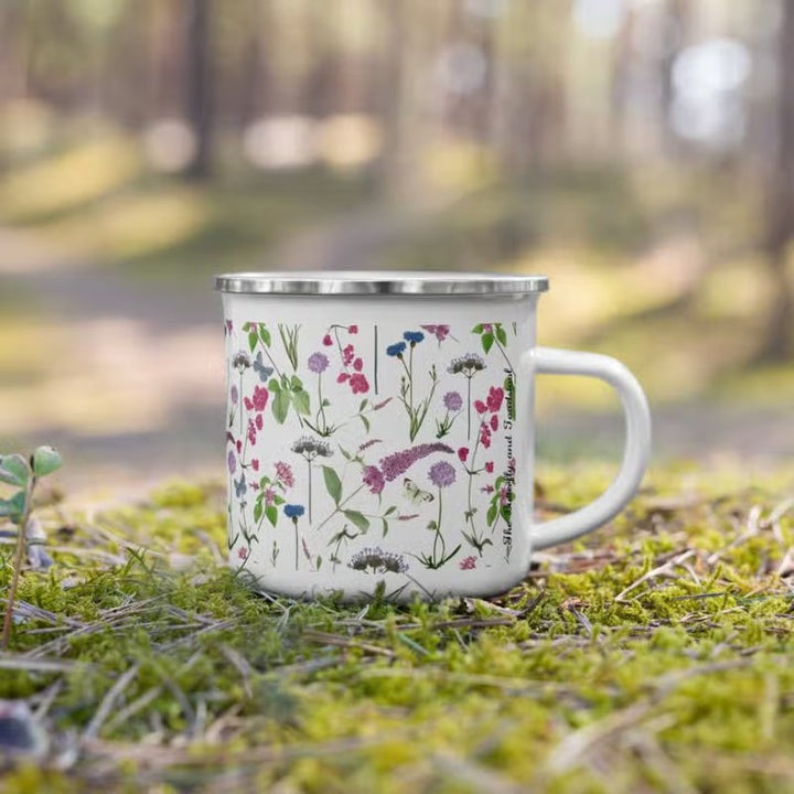 An enamel mug with watercolour-style wildflower design in a forest