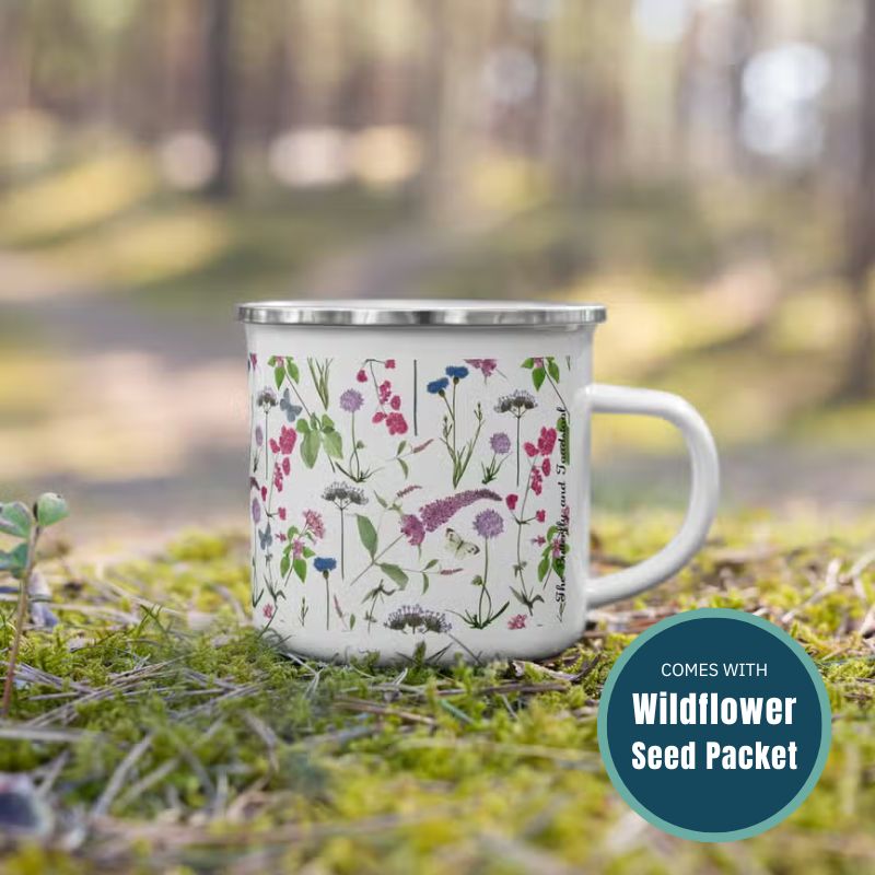 An enamel mug with watercolour-style wildflower design in a forest and text reading 'comes with wildflower seed packet'