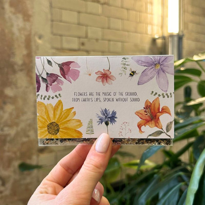 The front of a custom seed pocket with wildflower watercolour illustrations and a line of poetry