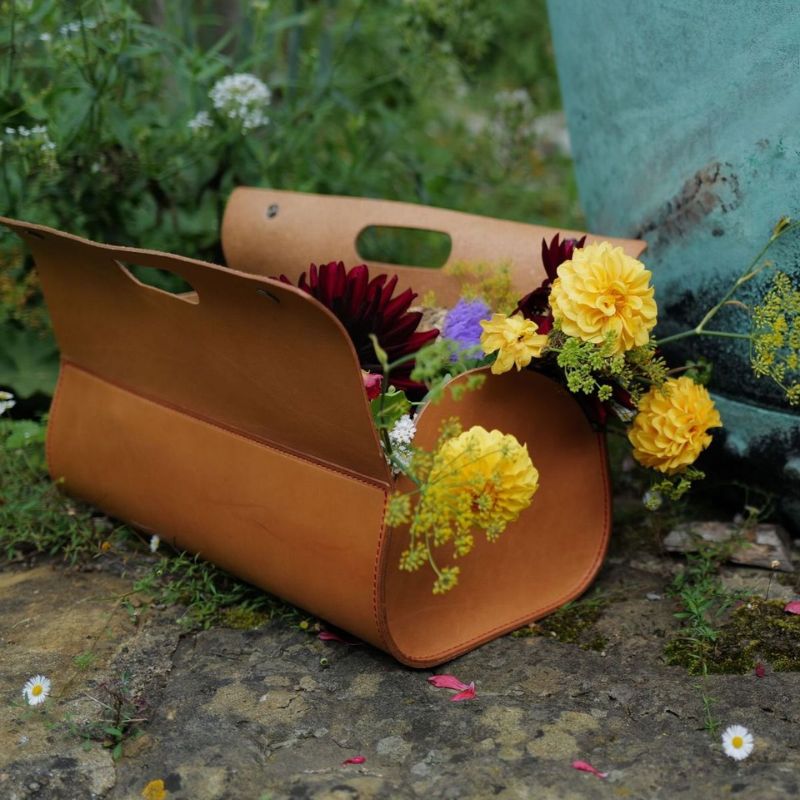 Brown leather Niwaki tool bag with flowers on a stone surface with greenery in the background